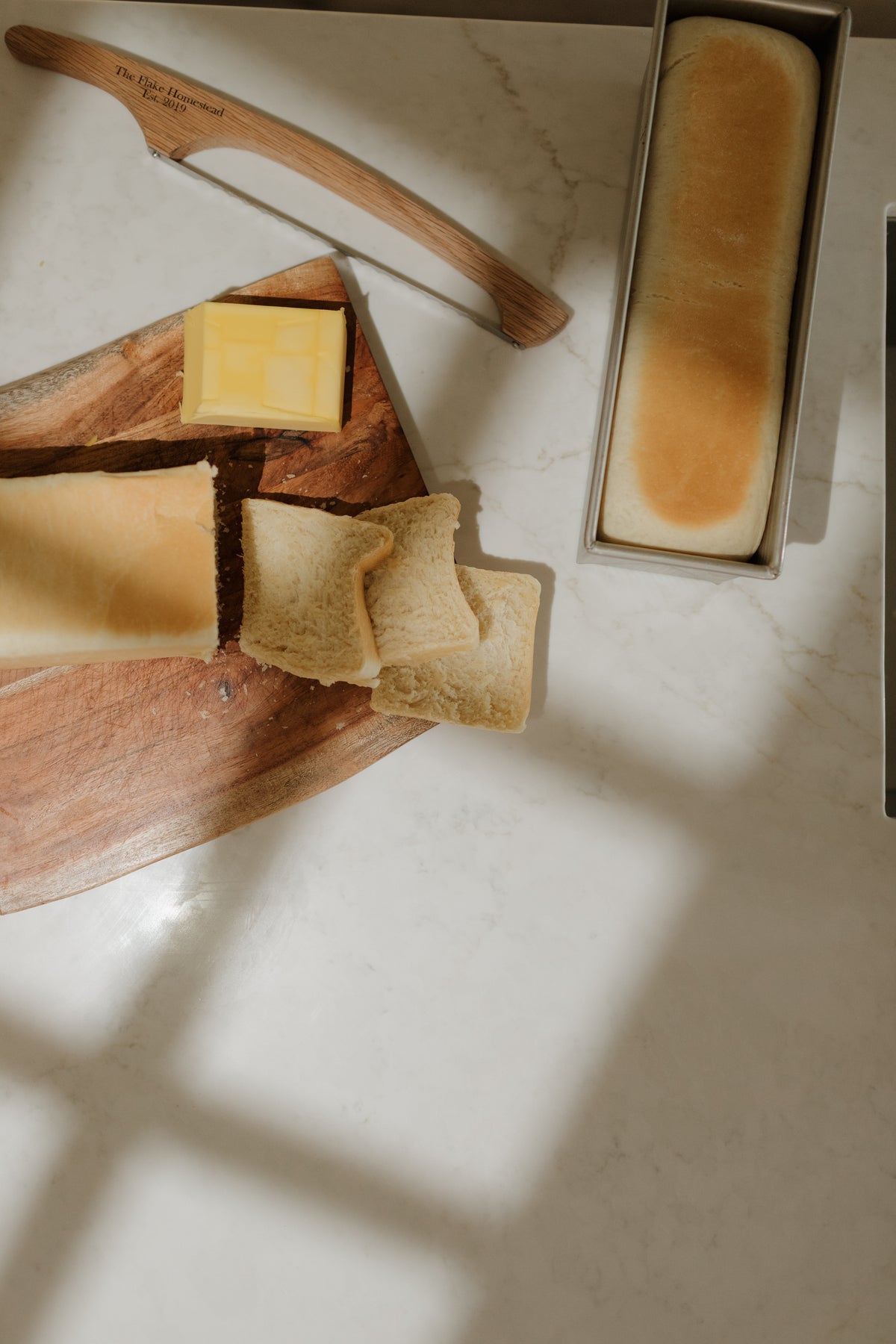 An overhead view of a sourdough board and loaf tin in window light