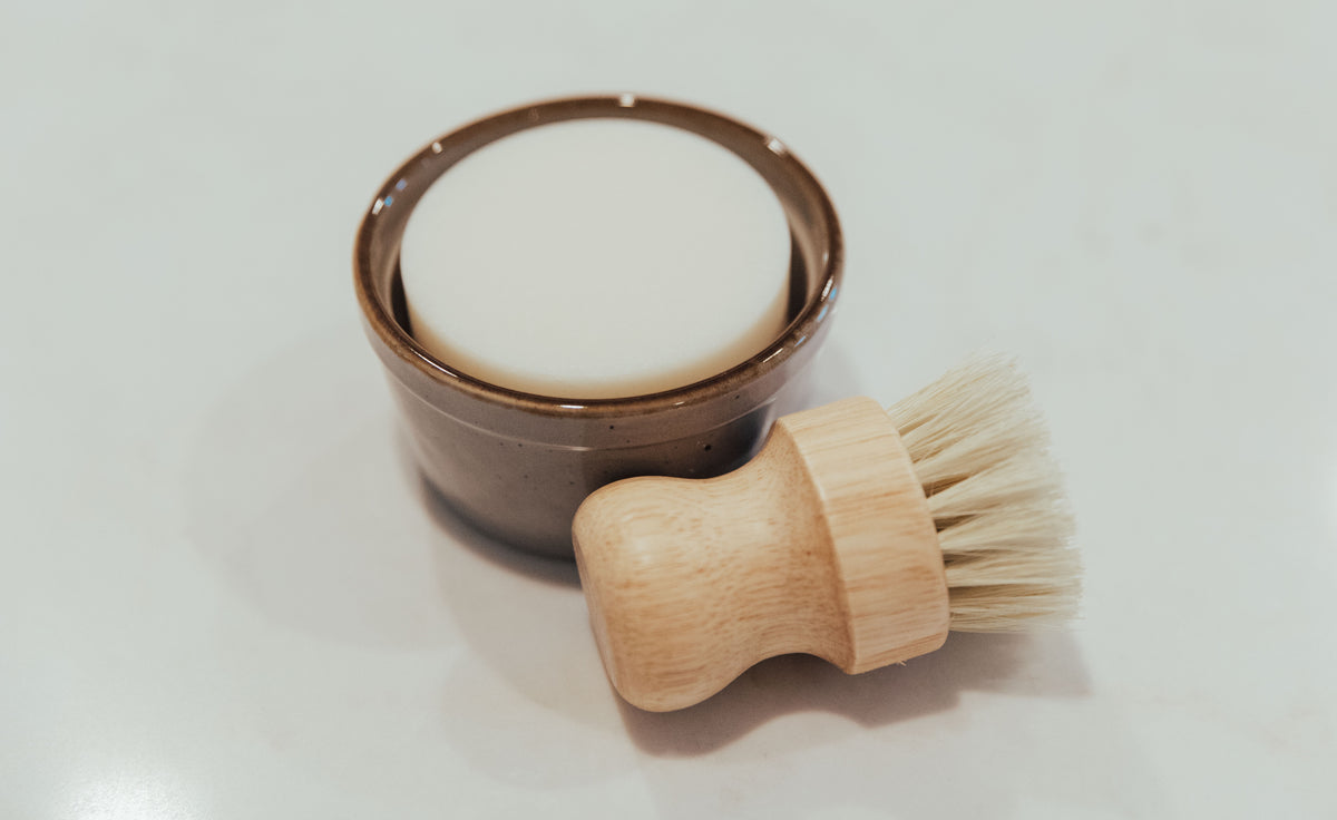 A ceramic dish and a bamboo brush on a white counter